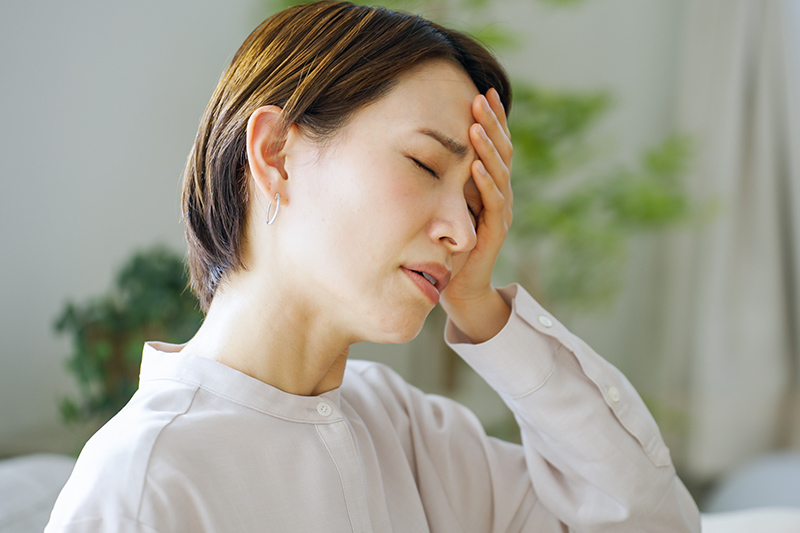 顔をしかめ額に手を当てる女性