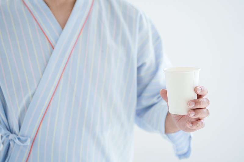 紙コップを持つ検査着姿の男性