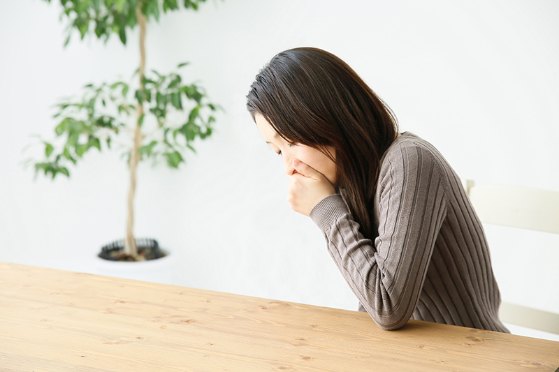 テーブルに肘をつき手で口元をおさえる女性